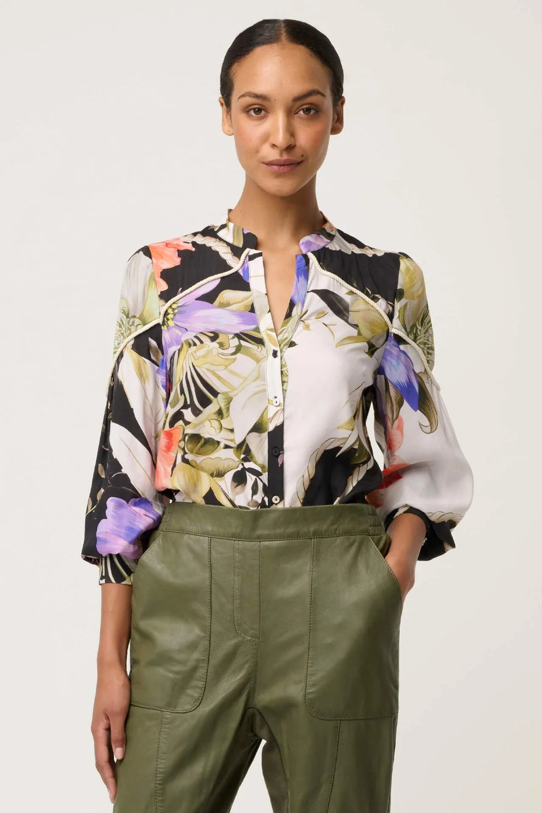 Woman wearing a floral blouse and green pants on a plain background