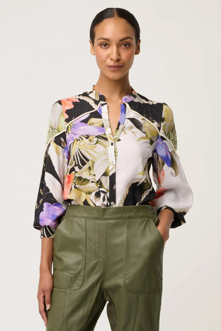 Woman wearing a floral blouse and green pants on a plain background