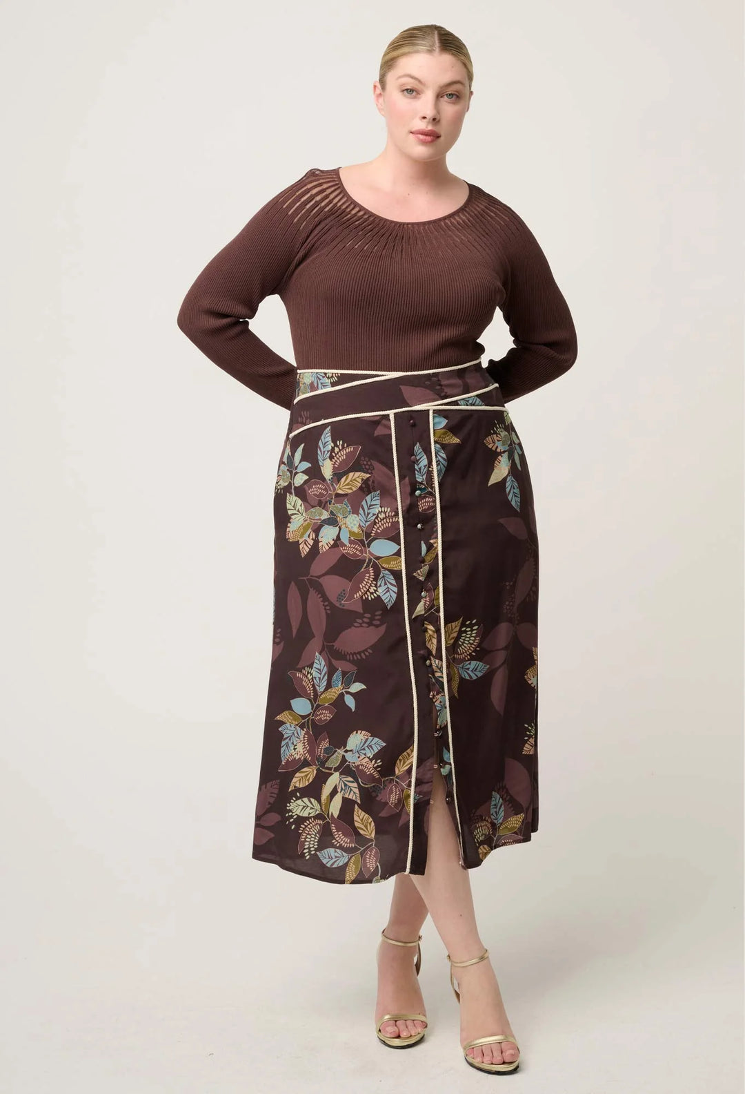 Woman wearing a brown top and floral skirt on a white background