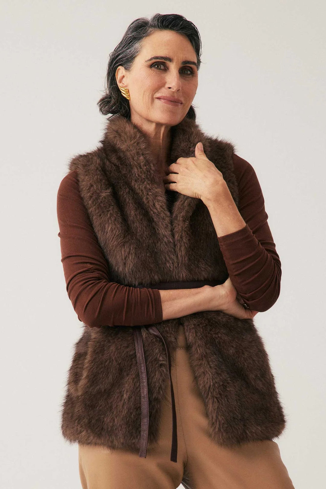 Woman wearing a brown fur vest over a brown shirt on a white background
