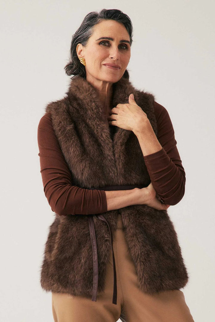 Woman wearing a brown fur vest over a brown shirt on a white background