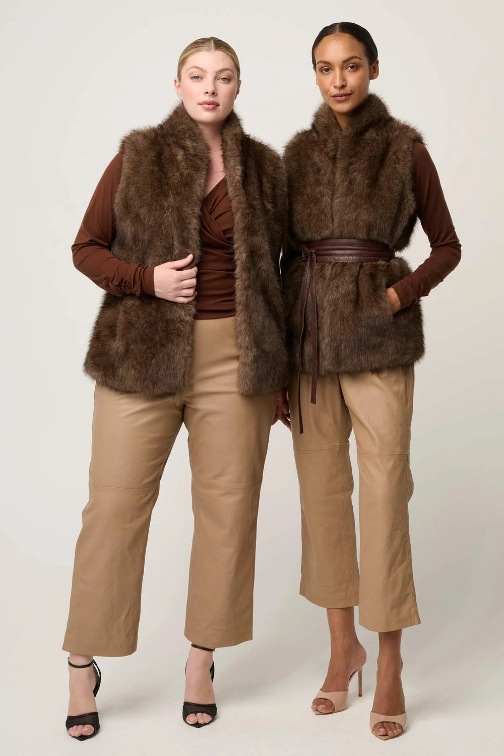 Two women wearing brown fur vests and beige pants on a white background