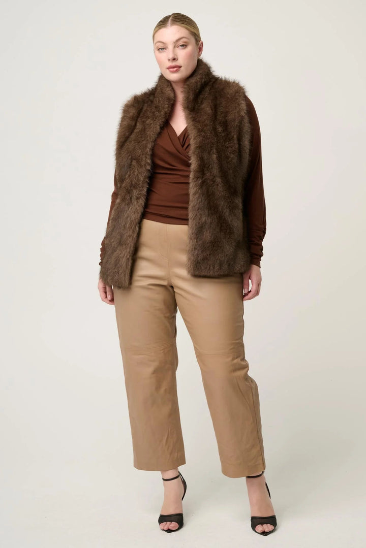 Woman wearing a brown fur coat, brown top, and beige pants on a white background
