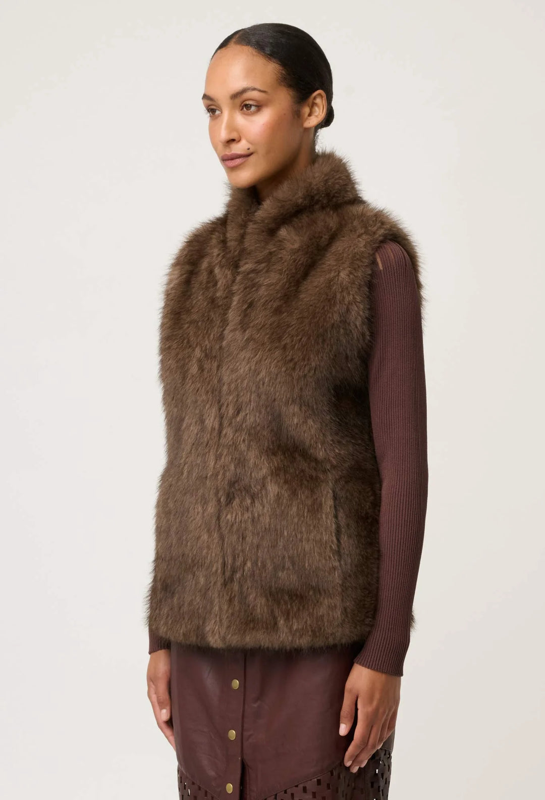 Woman wearing a brown fur vest against a plain background