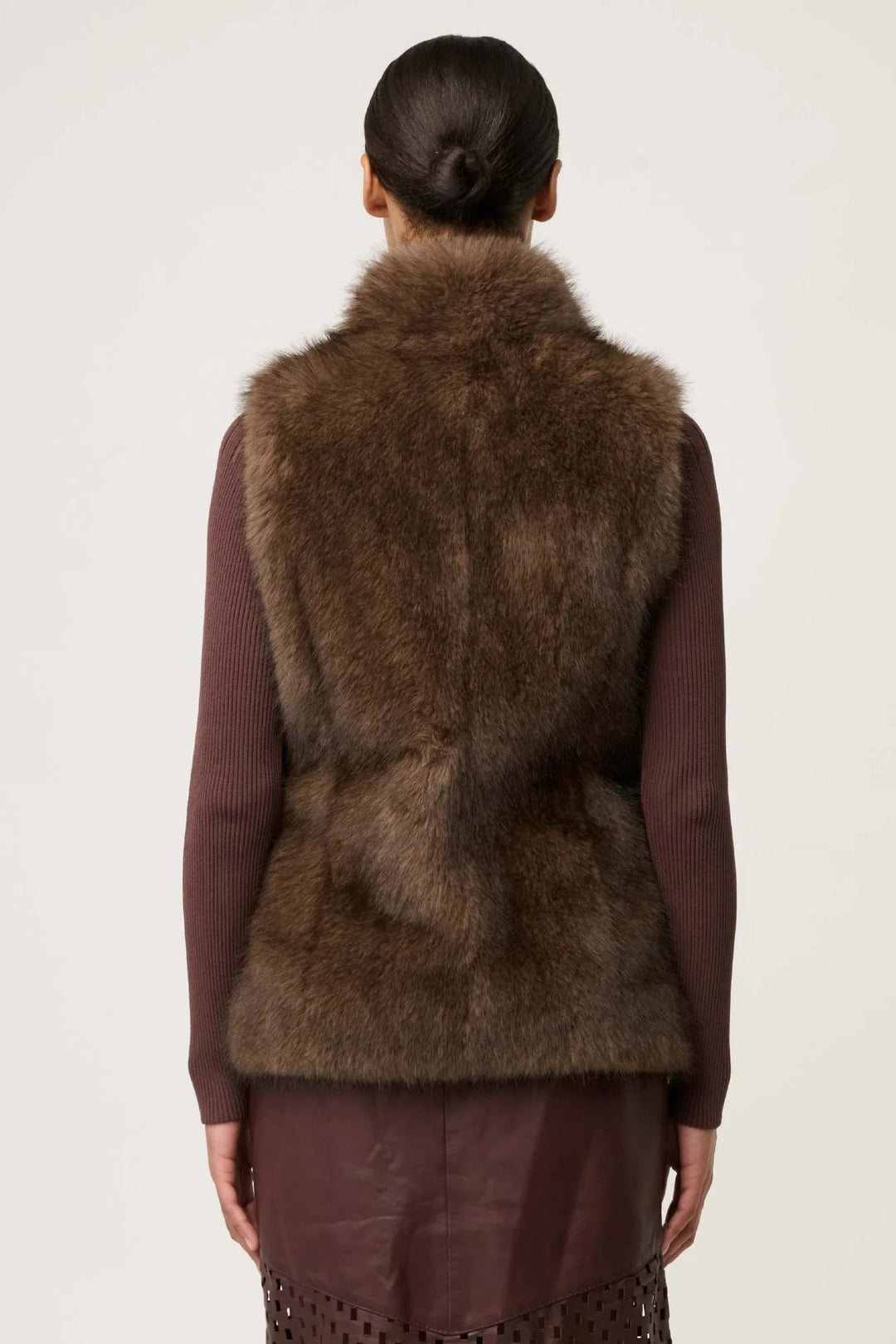 Person wearing a brown fur vest on a plain background