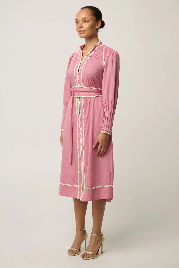A woman modeling a pink long-sleeve midi wrap dress with white contrast piping and a matching waist tie, paired with beige high-heeled sandals against a light gray studio background.