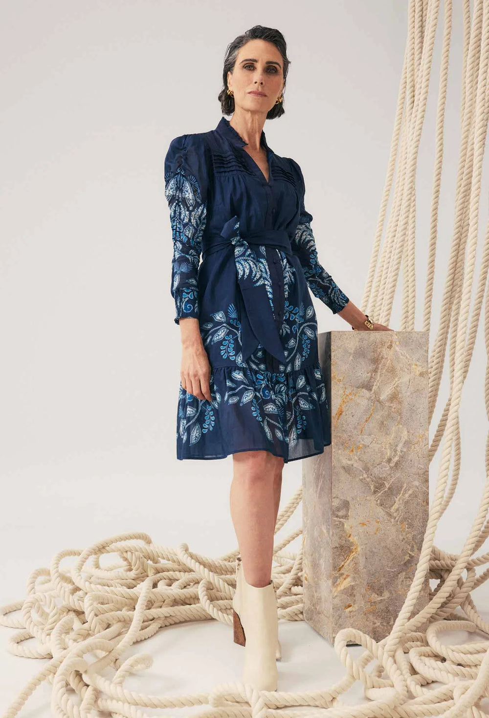 Woman in a blue dress standing next to a large stone block with ropes in the background