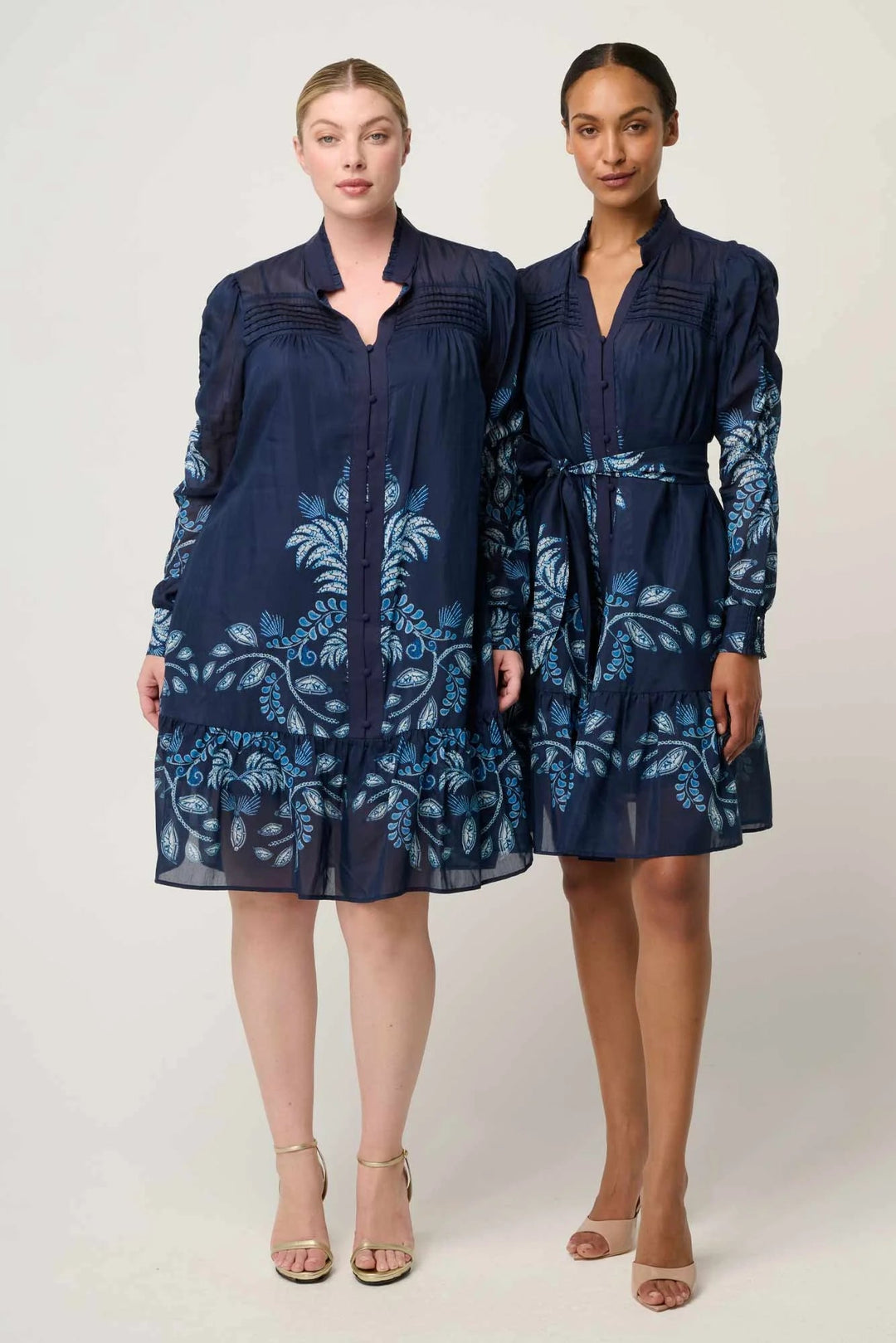 Two women wearing navy blue dresses with floral patterns on a white background