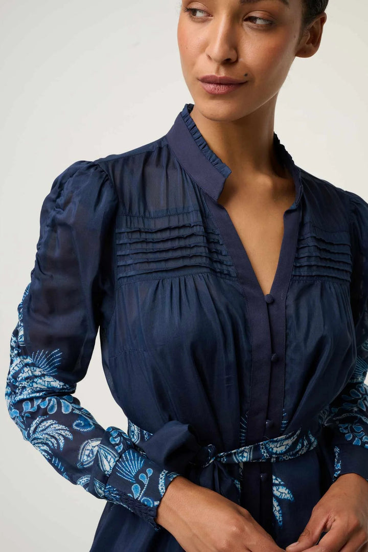 Woman wearing a navy blue blouse with floral cuffs on a white background