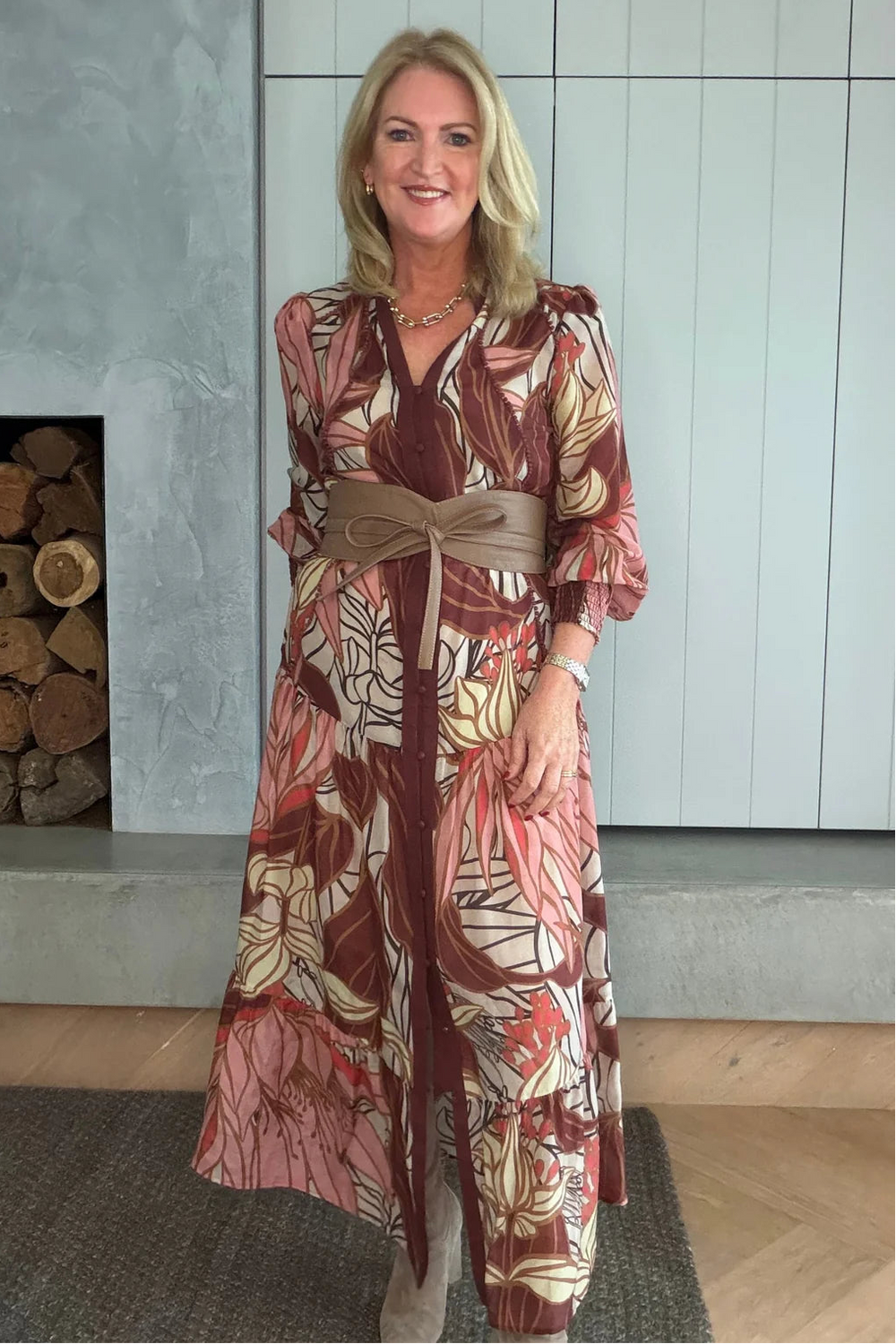 Woman wearing a patterned outfit standing in a room with a fireplace.