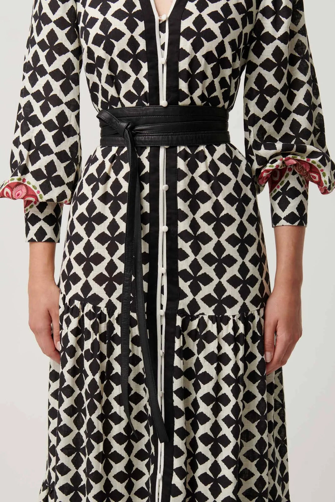 Long black and white patterned dress with a belt on a plain background
