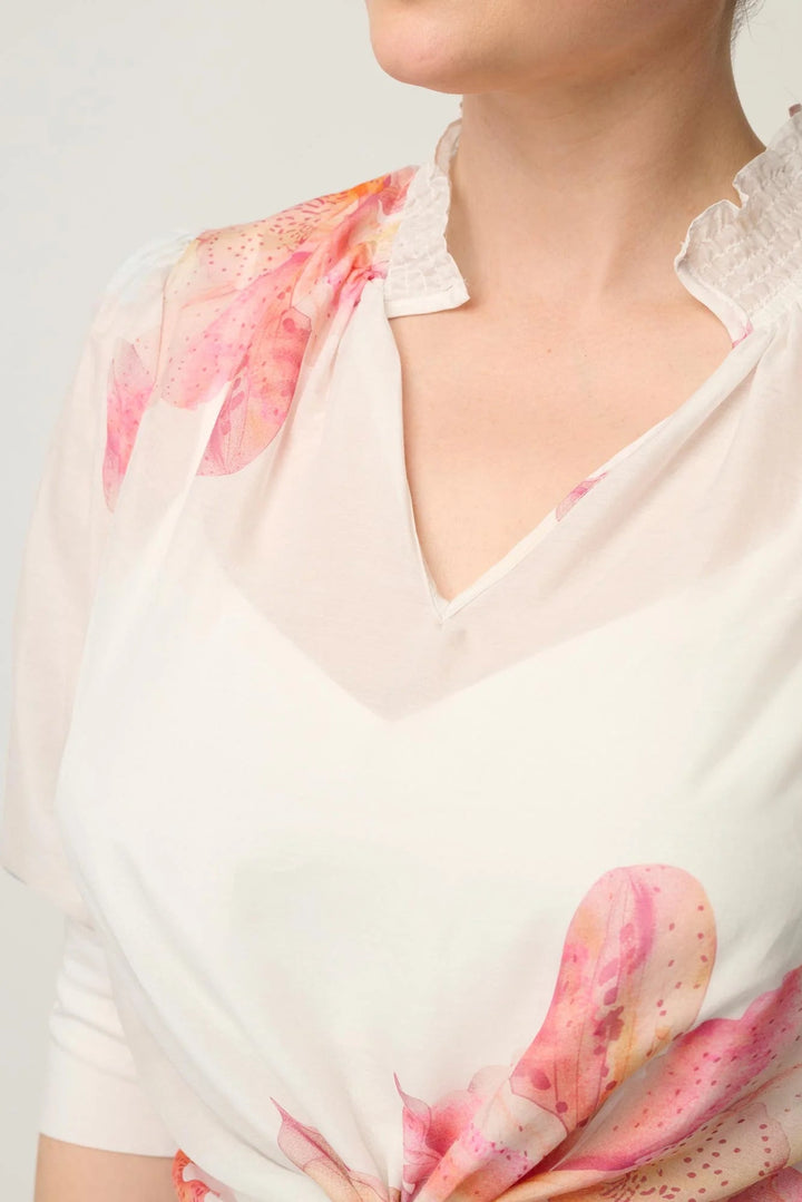 A close-up of a woman wearing a white blouse with pink and peach watercolor floral prints, featuring a ruffled collar.