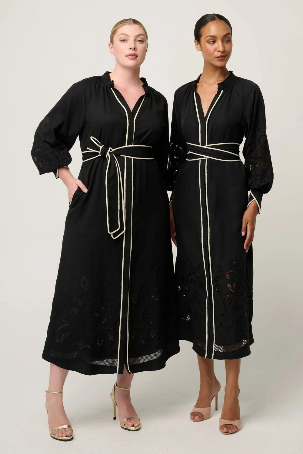 Two women wearing black long dresses with white trim on a white background