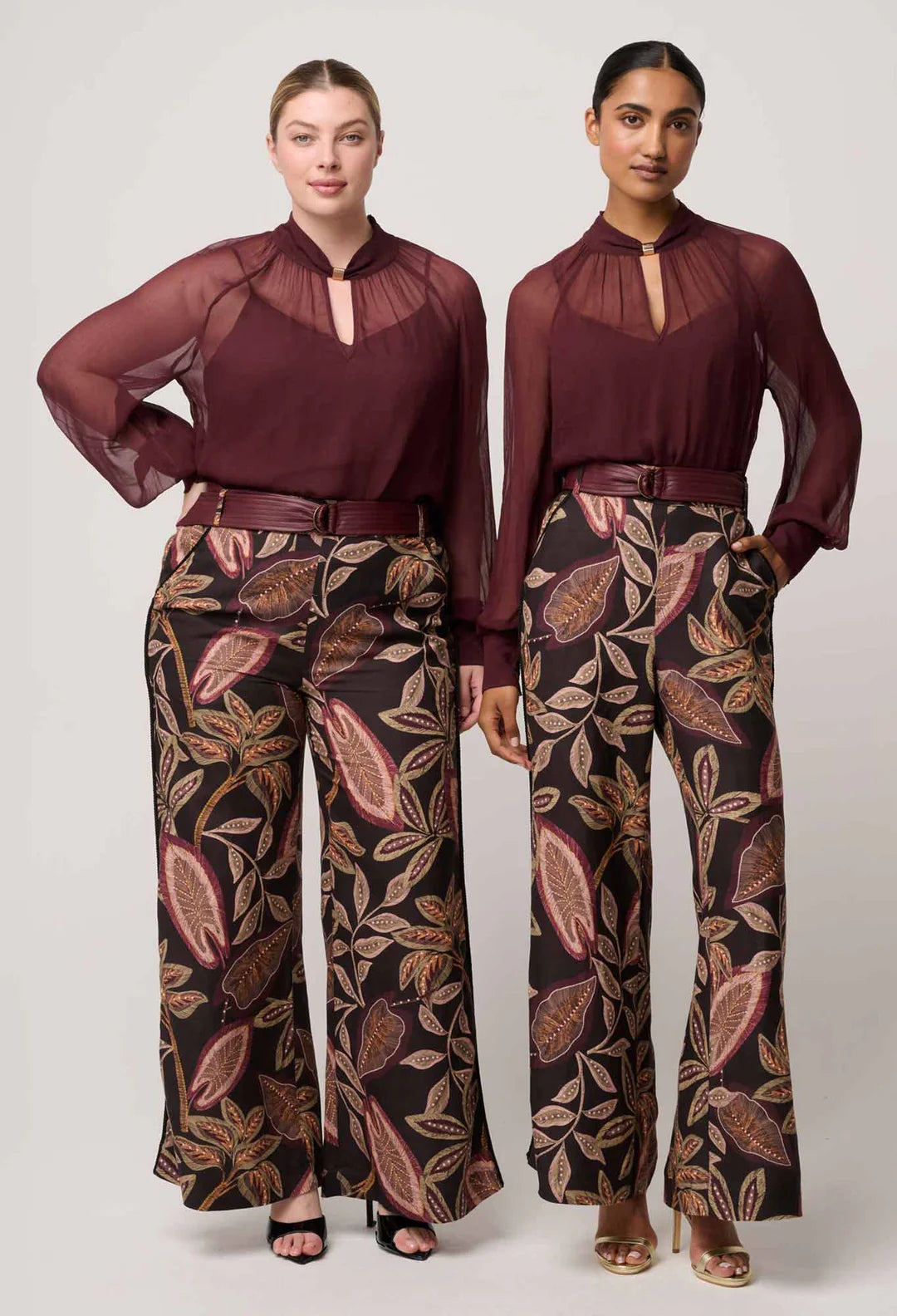Two women wearing matching outfits with burgundy tops and patterned pants on a white background