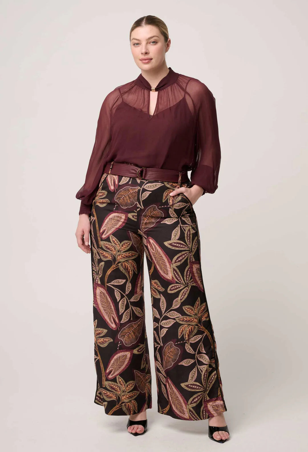 Woman wearing a burgundy blouse and patterned pants on a white background
