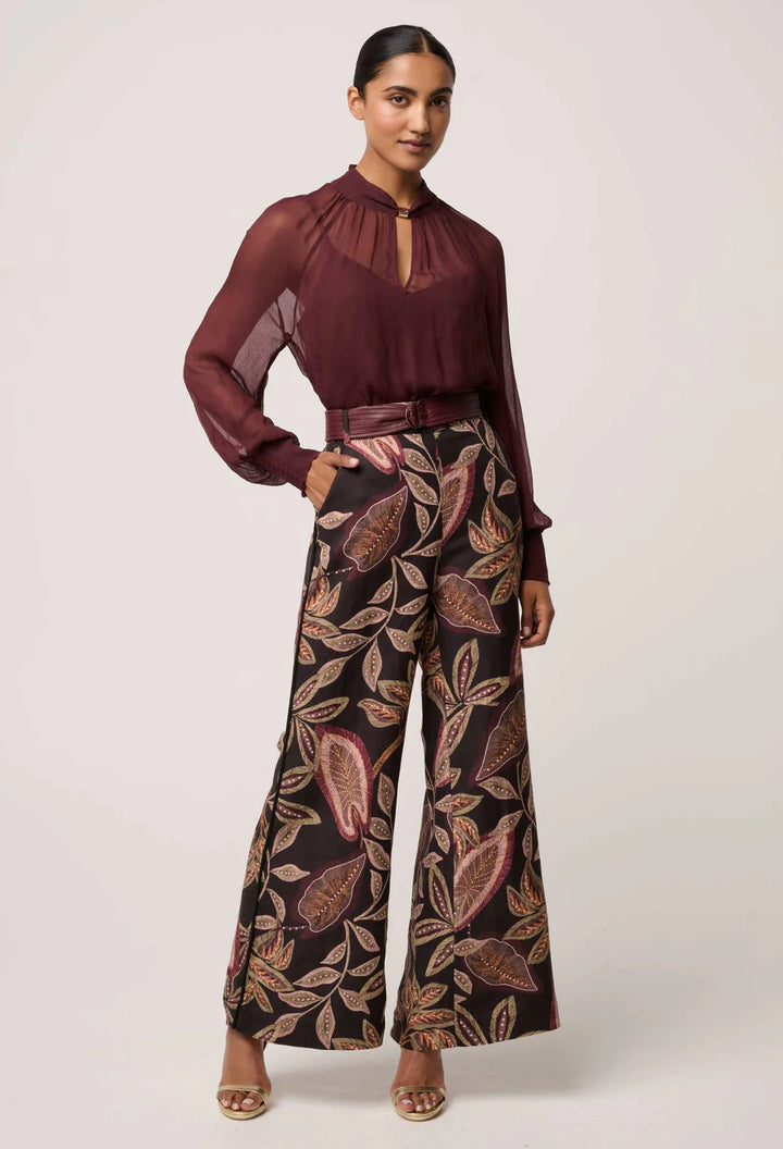Woman wearing a burgundy blouse and patterned pants on a white background