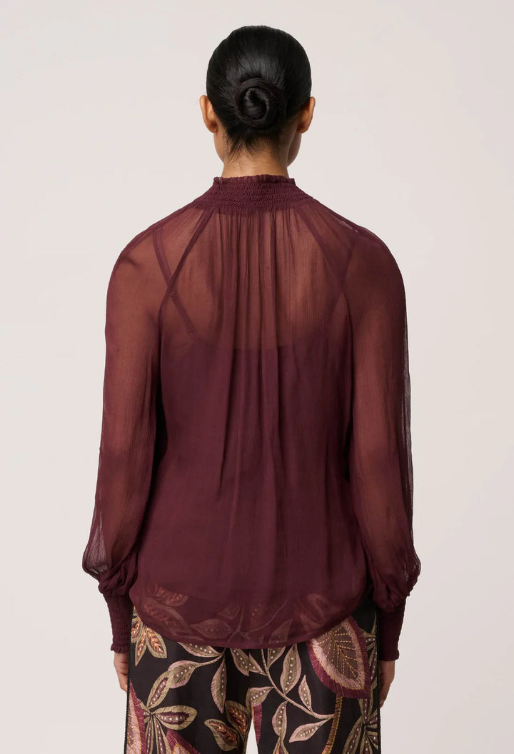 Person wearing a sheer burgundy blouse with a plain background