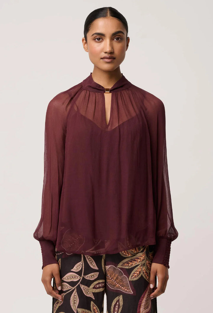 Woman wearing a burgundy blouse with sheer neckline against a white background