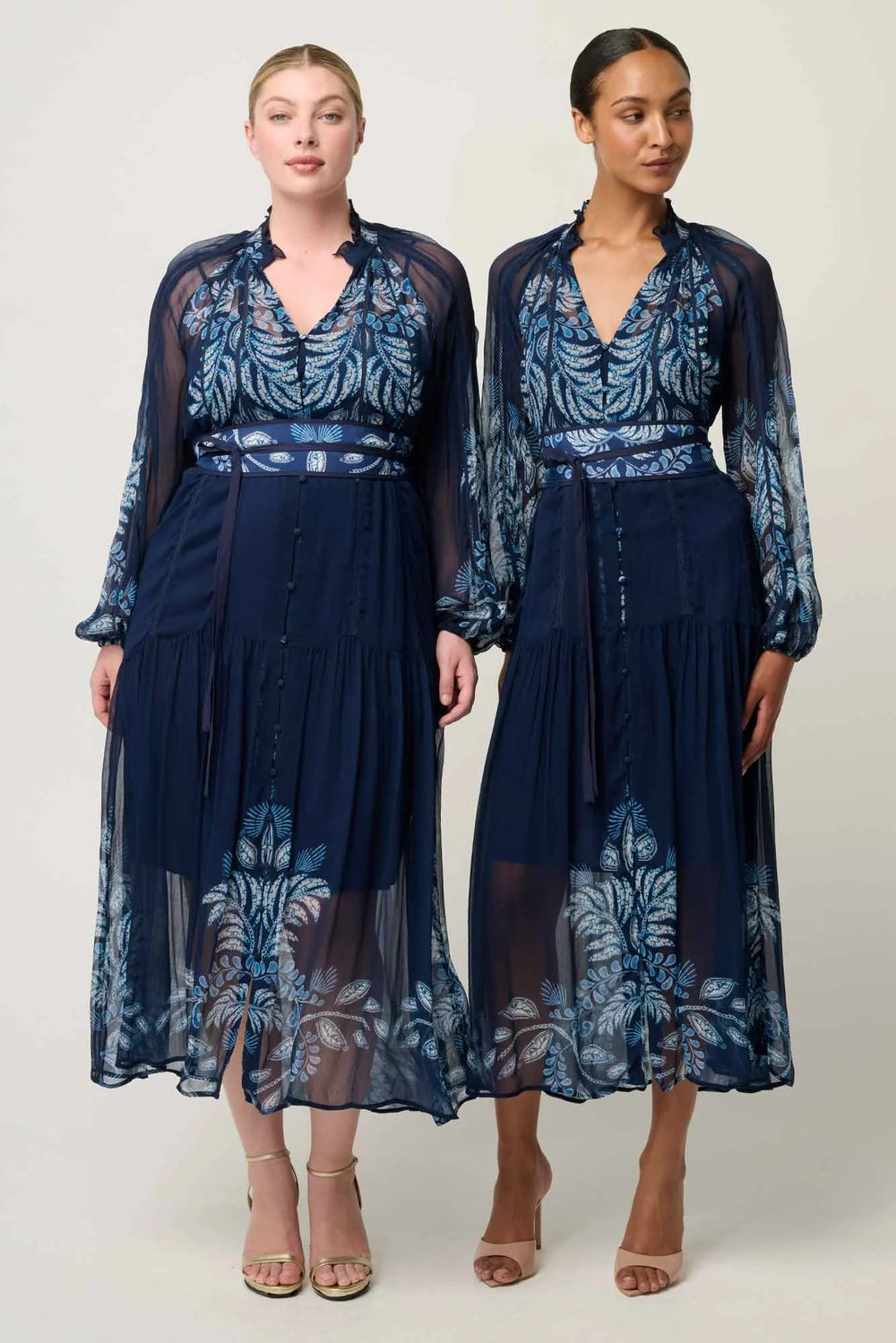 Two women wearing matching navy blue dresses with floral patterns on a white background