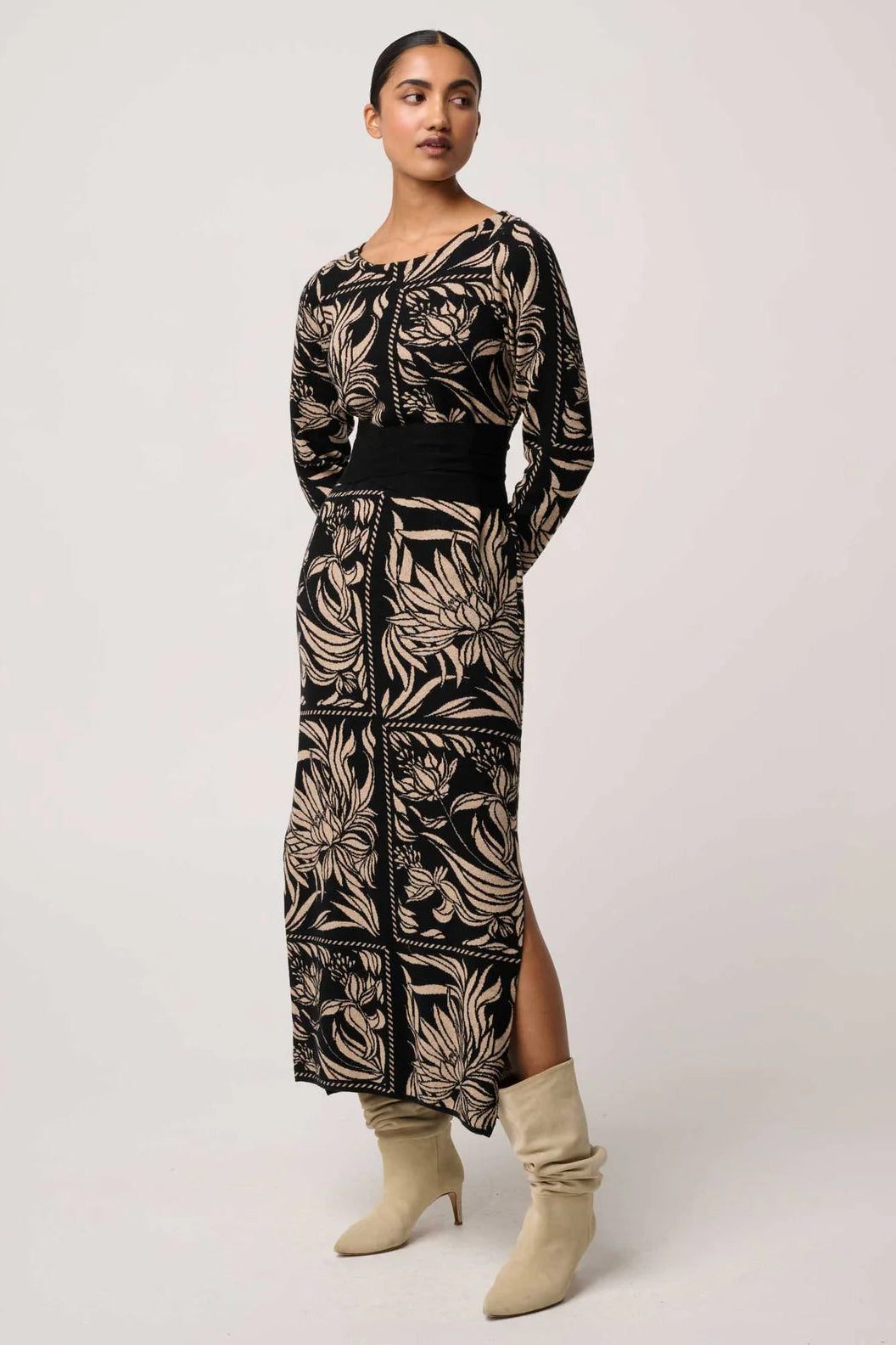Woman wearing a long, patterned dress with beige boots on a white background