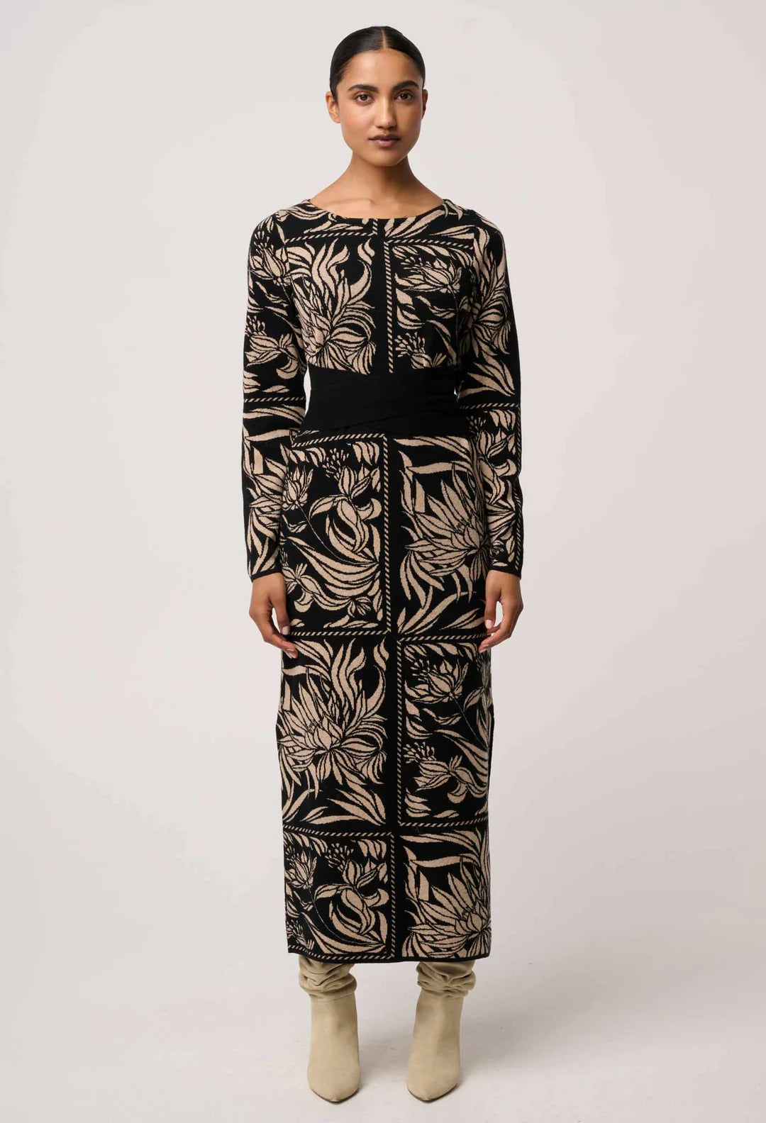 Woman wearing a long, patterned dress with a belt on a white background