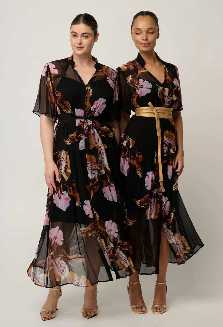 Two models wearing matching black midi dresses with a pink, brown, and beige floral print. The dress on the left is styled with sheer flutter sleeves and a tie waist, while the dress on the right features a gold belt and a high-low sheer hem.
