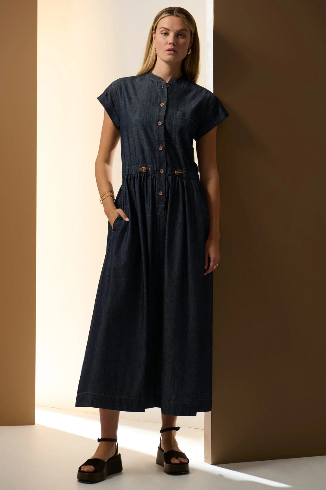 Woman wearing a dark blue dress standing against a brown wall. POL Muhle Denim Shirt Dress Indigo
