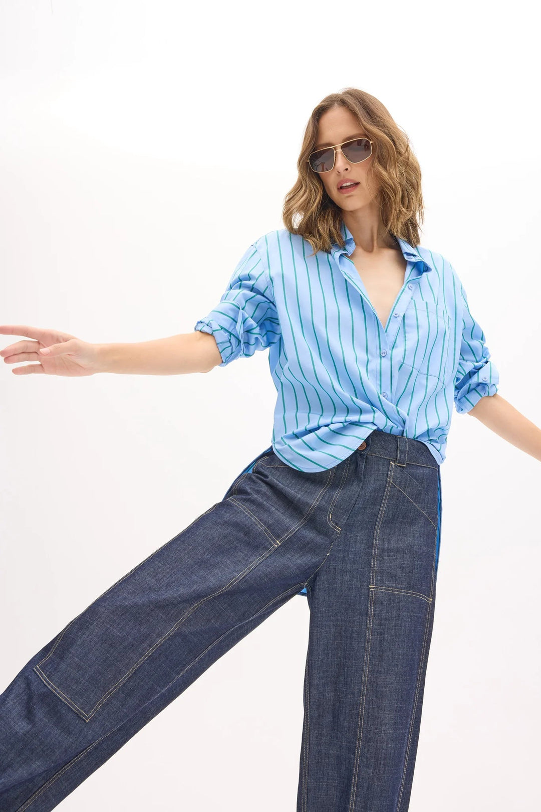 Woman wearing a light blue striped shirt and dark blue jeans on a white background