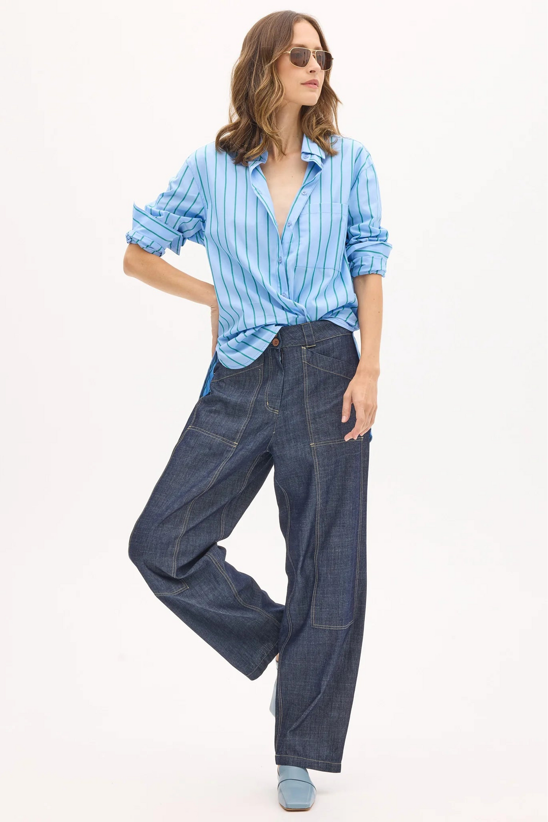 Woman wearing a blue striped shirt and dark jeans on a white background