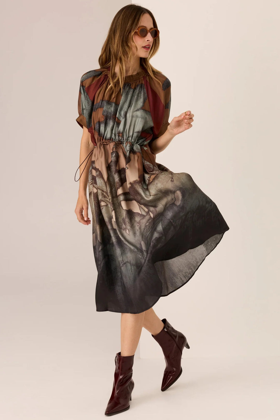 Woman wearing a patterned dress and brown boots on a plain background