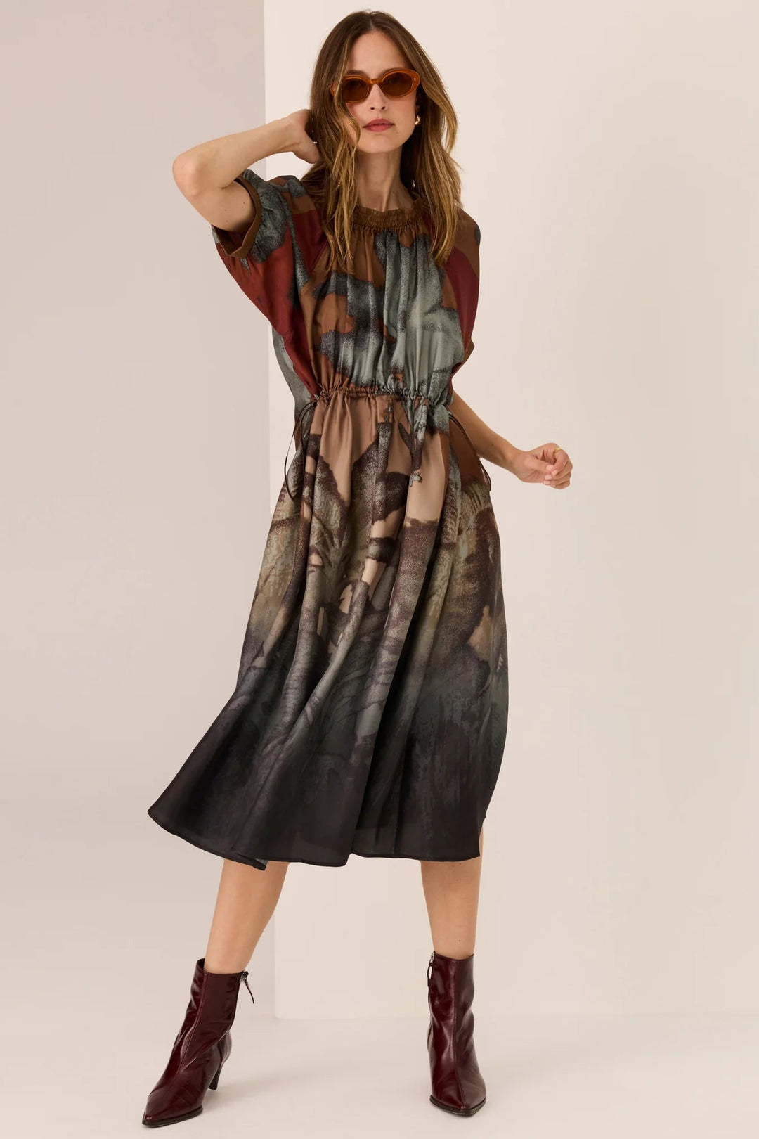 Woman wearing a patterned dress with maroon boots on a beige background