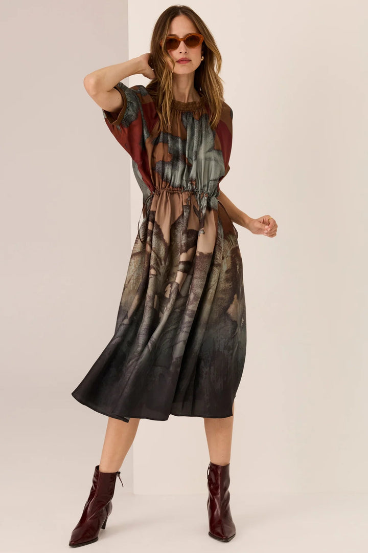 Woman wearing a patterned dress with maroon boots on a beige background