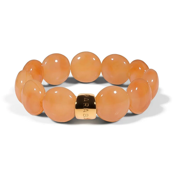 A beaded stretch bracelet featuring smooth, round peach-orange beads and a polished gold-tone metal clasp engraved with the brand name 'ARABIA'.