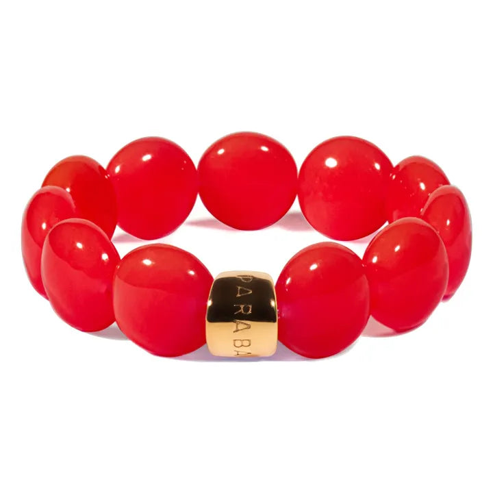 A red beaded stretch bracelet with a polished gold-toned metal spacer engraved with the brand name 'PARABRA'.
