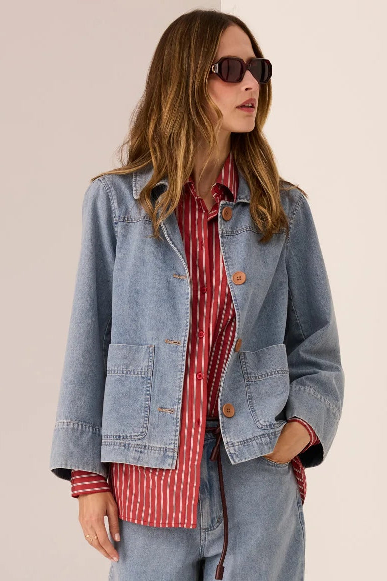 Woman wearing a denim jacket, red striped shirt, and blue jeans on a beige background