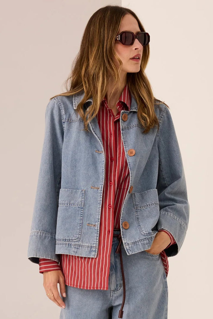 Woman wearing a denim jacket, red striped shirt, and blue jeans on a beige background