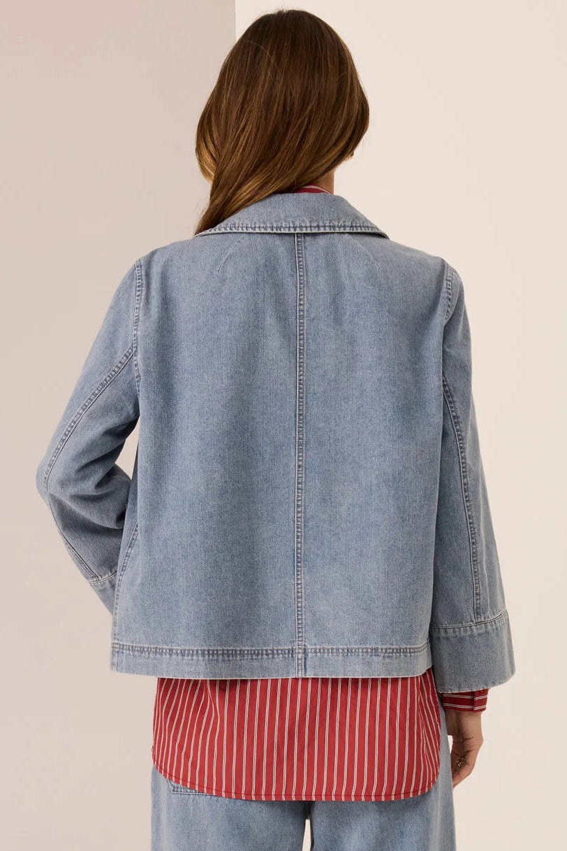 Person wearing a denim jacket and pants with a red striped shirt on a plain background