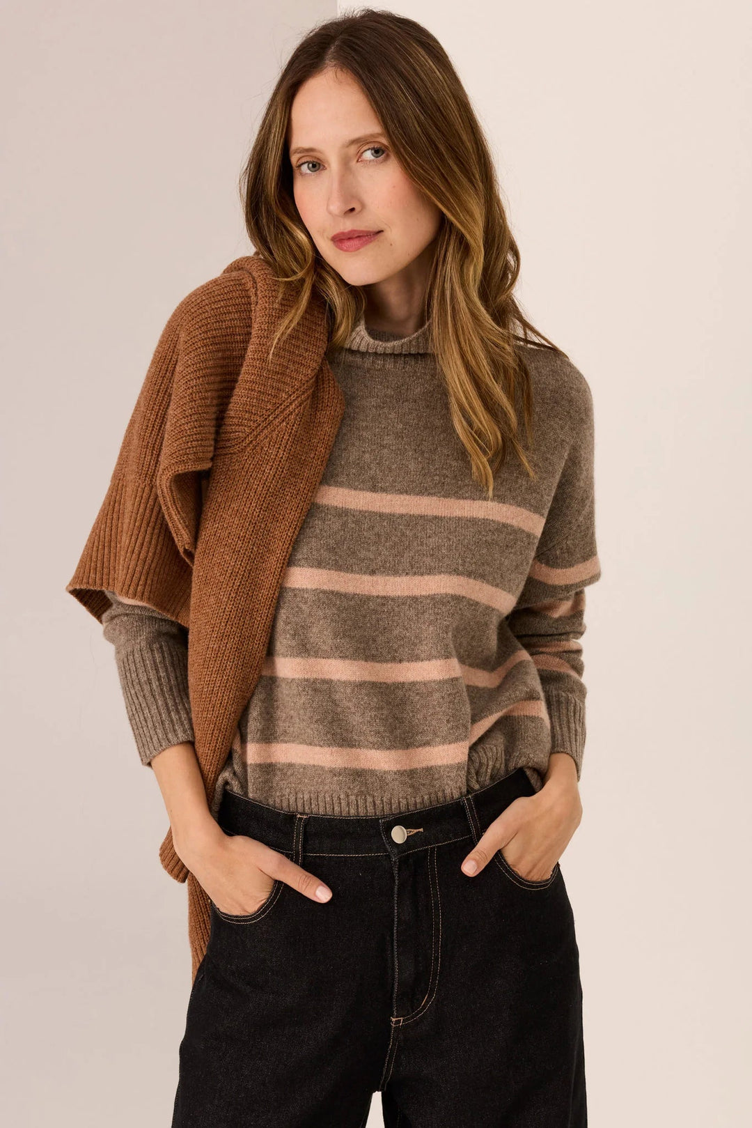 Woman wearing a brown sweater with a striped pattern and a brown cardigan on a beige background