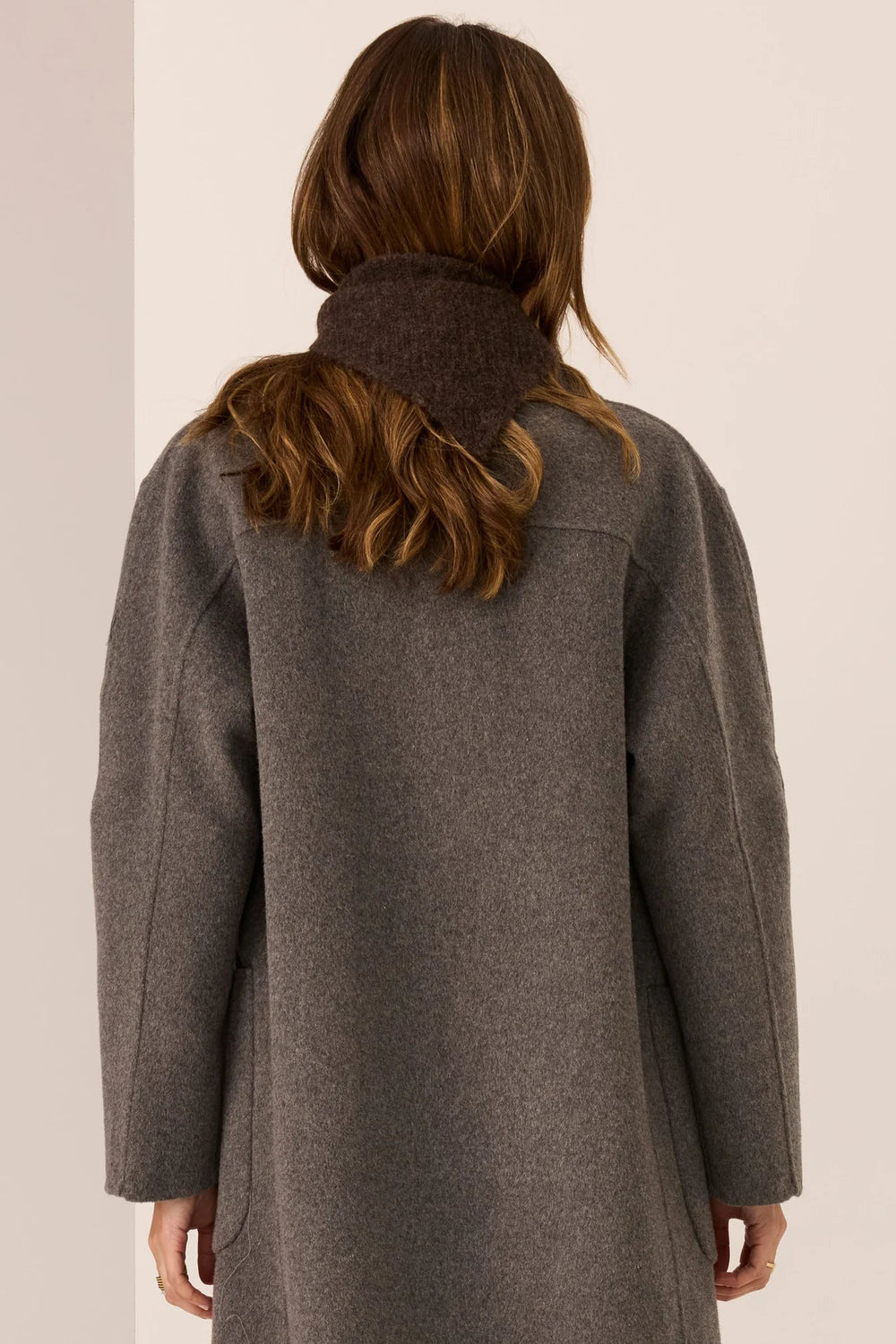 Person wearing a gray coat with a plain background