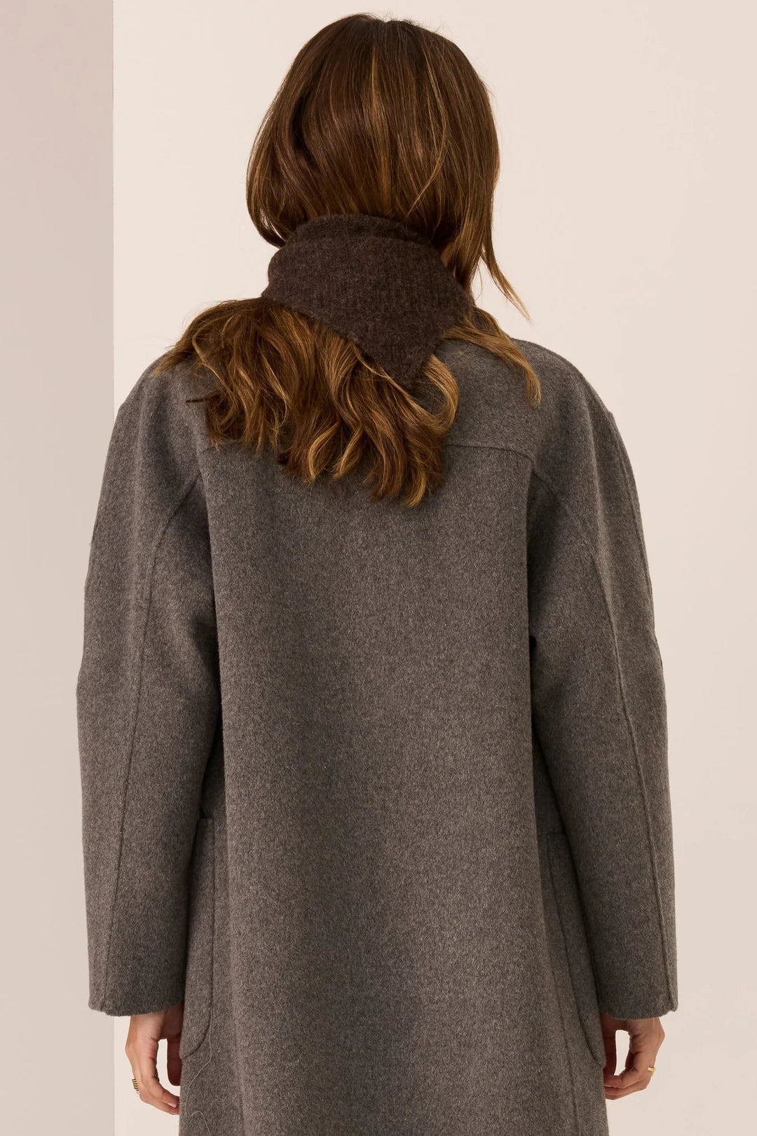 Person wearing a gray coat with a plain background