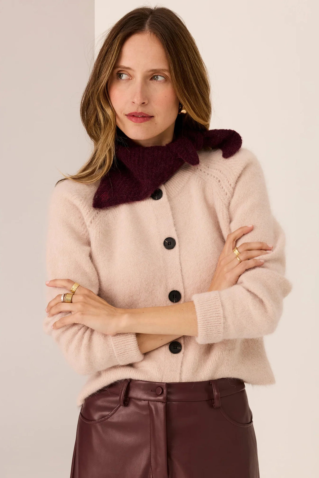 Woman wearing a beige sweater with black buttons and a burgundy scarf against a light background