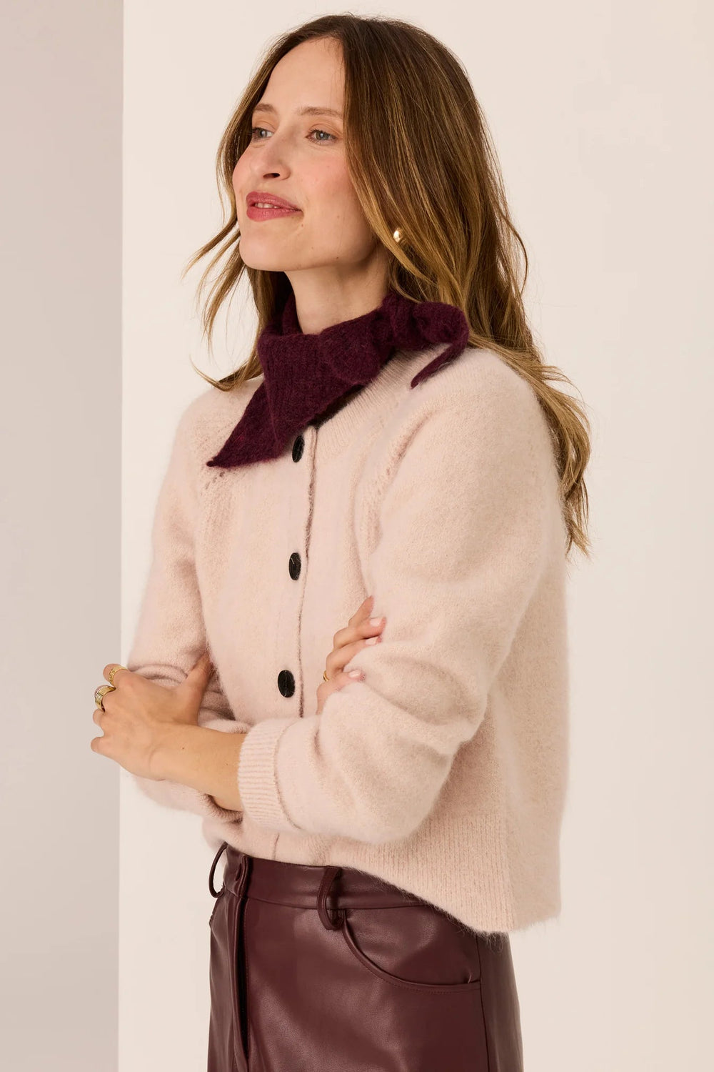 Woman wearing a beige sweater with a dark purple scarf against a light background