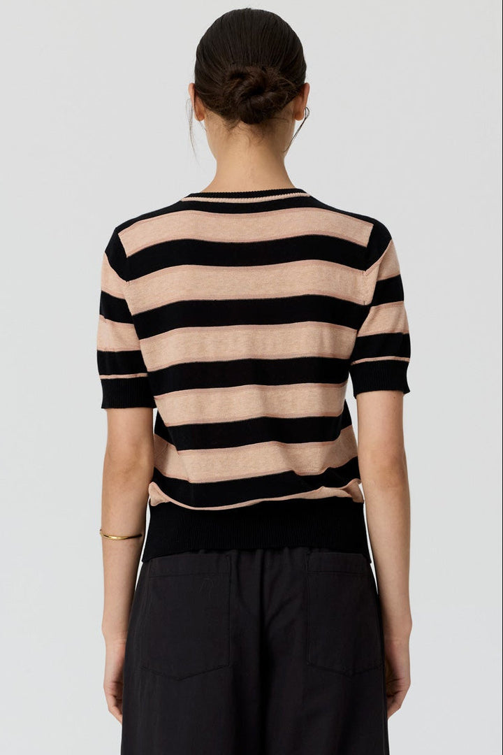 A woman viewed from the back wearing a beige and black horizontally striped short-sleeve knit top with black wide-leg trousers, against a light gray studio background.