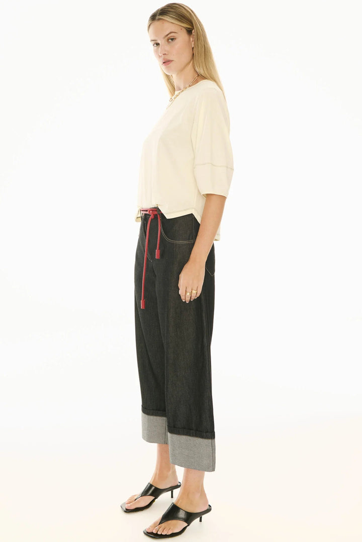 Woman wearing a cream top and black pants with a red belt on a white background