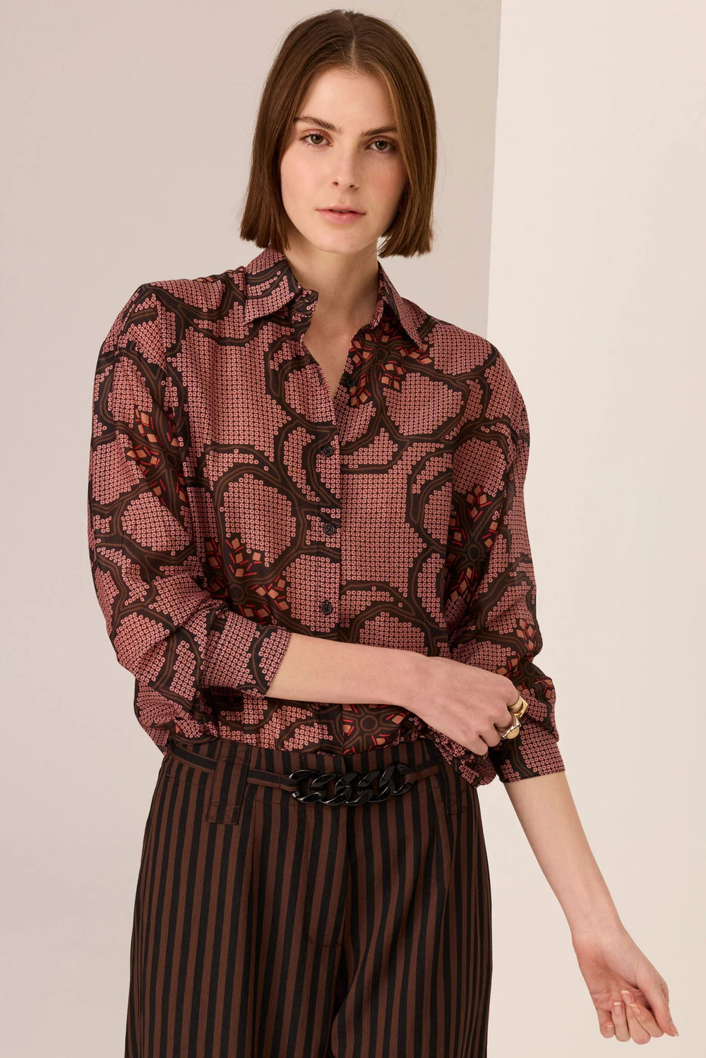 Woman wearing a patterned blouse and striped skirt against a plain background