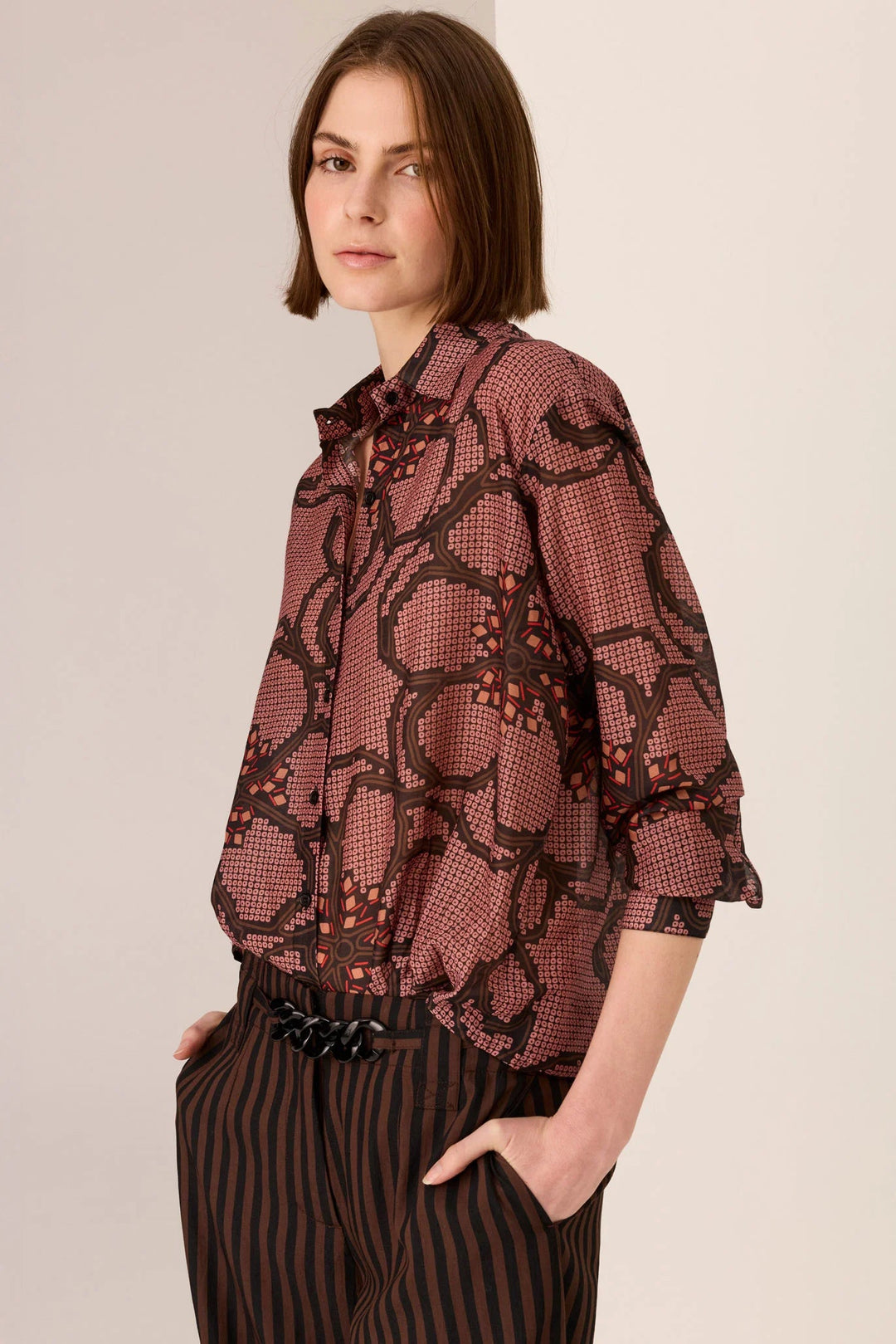 Woman wearing a patterned blouse and striped pants against a plain background