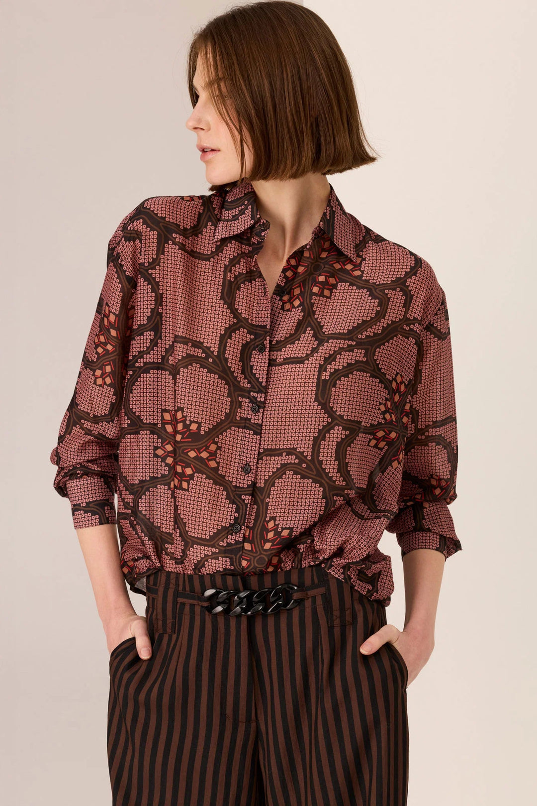 Woman wearing a patterned blouse and striped pants on a beige background