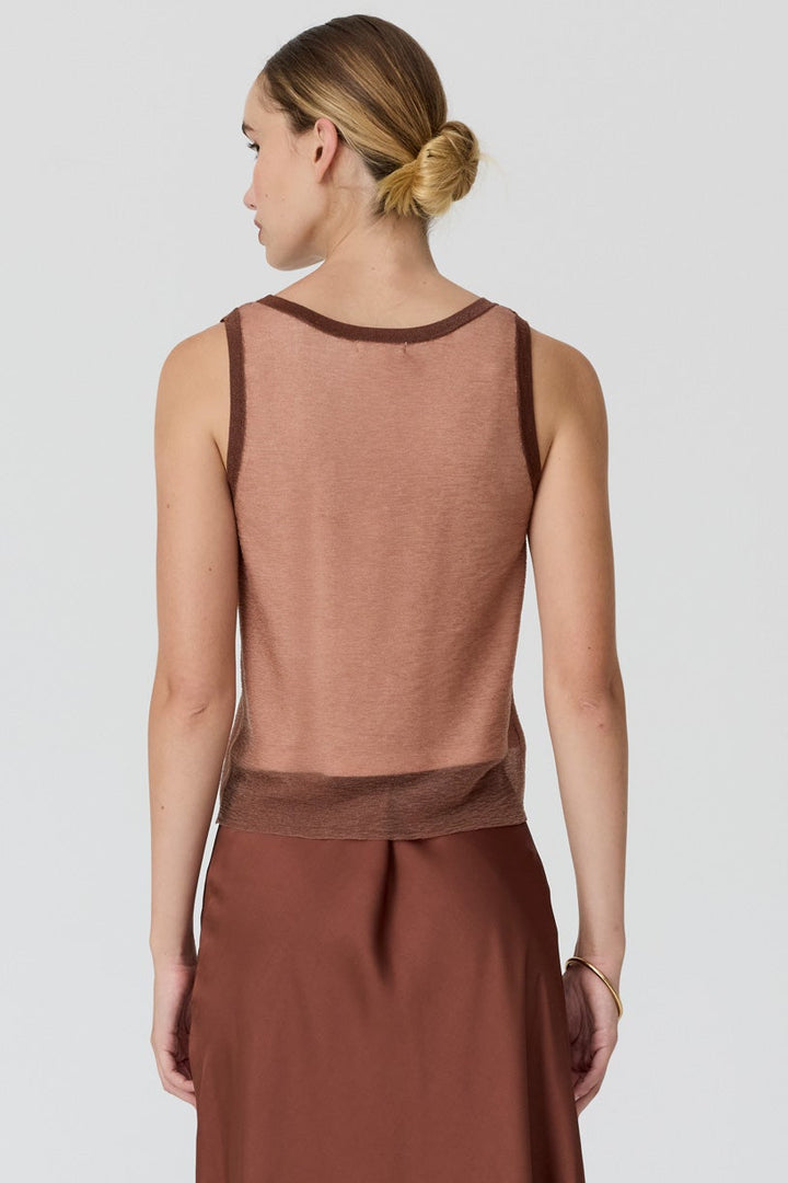 A woman shown from the back wearing a sleeveless rust-brown dress with a sheer upper yoke and a long flowing skirt, photographed against a light gray studio background.