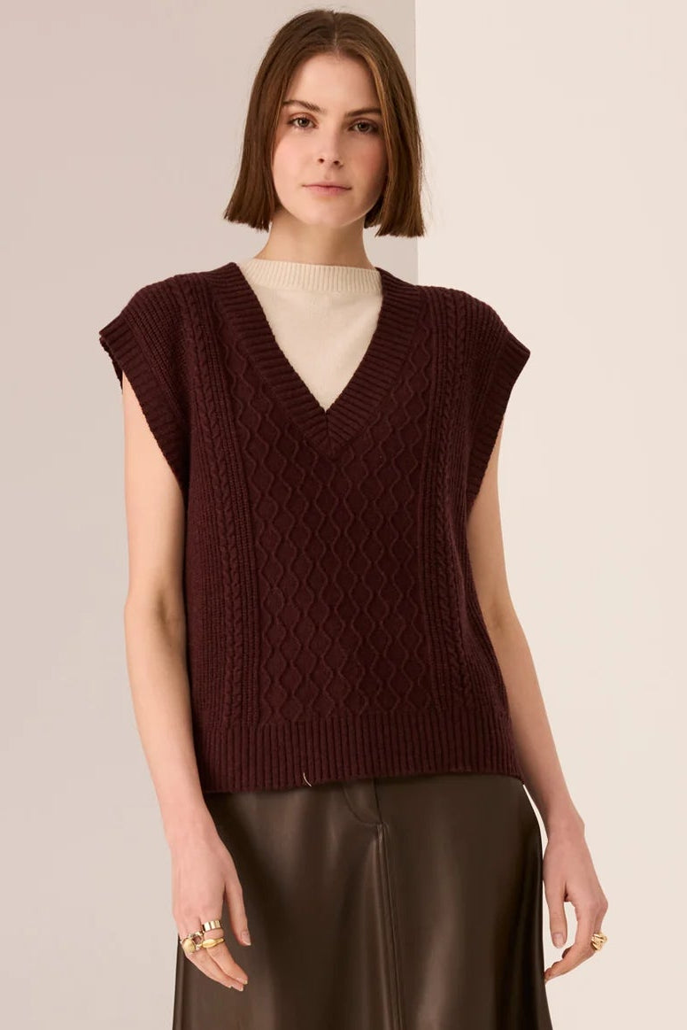 Woman wearing a brown sleeveless top and leather skirt with burgundy boots on a beige background