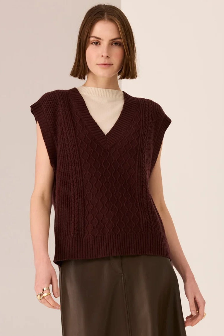 Woman wearing a brown sleeveless top and leather skirt on a beige background